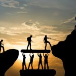 people helping each other cross the bridge between two cliffs